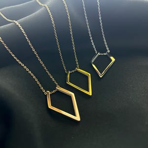 Puede incluir: Tres delicados collares de oro, plata y oro rosa con colgantes en forma de diamante. Los collares se muestran sobre un fondo de tela negro.