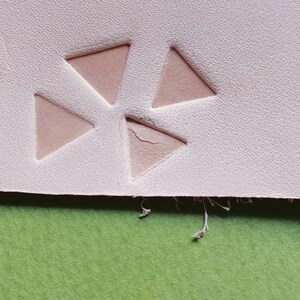 Könnte beinhalten: Ein blassrosa Materialbogen mit drei dreieckigen Ausschnitten, die in einer Gruppe angeordnet sind. Die Oberfläche hat ein strukturiertes Aussehen und einer der dreieckigen Ausschnitte weist einen kleinen Riss an der Kante auf, mit losen Fasern darunter.