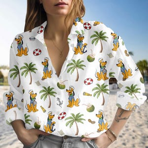 Puede incluir: Camisa blanca con botones con un estampado repetido de Pluto el perro con atuendo de marinero, palmeras, cocos, anclas y salvavidas. La camisa de manga larga tiene un cuello clásico y cierre de botones.