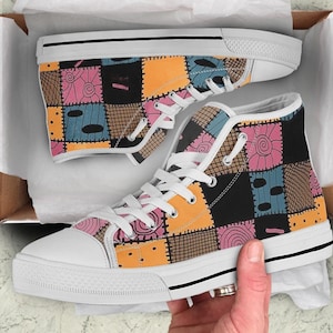 以下が含まれることがあります： カラフルなパッチワークのデザインが施された白いハイカットキャンバスシューズ。デザインには、オレンジ、ピンク、ブルー、ブラックなど、さまざまな色とパターンが使用されています。