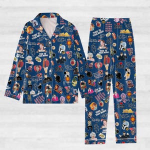 Puede incluir: Conjunto de pijama azul con un patrón repetido de imágenes y texto. La parte superior de manga larga y los pantalones presentan varias ilustraciones y frases, incluyendo "This is Tha Wah" y "Pedro Pascal". El conjunto tiene ribetes blancos.