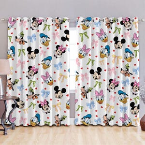 Puede incluir: Cortinas blancas con un patrón repetido de personajes de Disney, incluyendo Mickey Mouse, Minnie Mouse, Donald Duck, Goofy y Pluto. Los personajes llevan lazos y corazones coloridos.