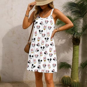 Puede incluir: Vestido de verano blanco con un estampado repetido de caras de Minnie Mouse, Daisy Duck y Mickey Mouse. El vestido tiene tirantes finos y un escote redondo. El vestido llega a la rodilla y es adecuado para el clima cálido.