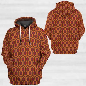 Op de afbeelding: Een hoodie met een herhalend geometrisch patroon in tinten oranje, bruin en rood. Het ontwerp bedekt het hele kledingstuk, inclusief de capuchon. De hoodie heeft een trekkoord en een voorzak.