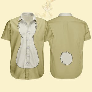 Puede incluir: Camisa de manga corta color beige con un diseño blanco y beige. La parte delantera de la camisa tiene un panel blanco en el centro, y la parte trasera tiene un diseño circular blanco. Un conejo de dibujos animados está en el fondo.