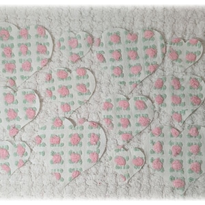 May include: A white, textured surface with ten heart-shaped appliqués. Each heart features a pattern of pink roses and green leaves on a white background. The hearts are arranged in a grid-like pattern.