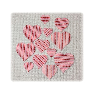 May include: A collection of eleven heart-shaped fabric cutouts arranged on a white textured square base. Each heart features a pattern of vertical stripes in alternating shades of red, light pink, and white, with varying sizes throughout.
