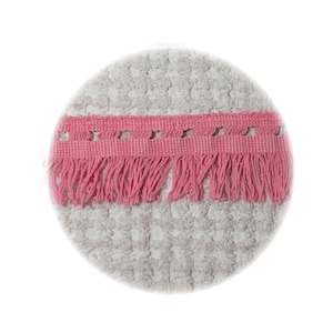 May include: A circular, light gray textured fabric coaster featuring a horizontal strip of pink woven trim across the center. The pink trim includes a row of small square cutouts along the top edge and a fringe of hanging threads along the bottom.