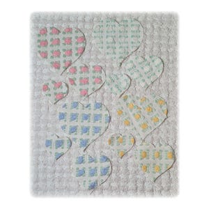 May include: A white, textured background with appliqued heart shapes in various sizes. The hearts feature floral patterns in pink, blue, and yellow, creating a soft, romantic aesthetic. The overall design is reminiscent of a handmade quilt.