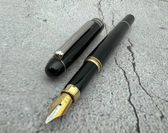 May include: A black and silver fountain pen with a gold nib. The pen is on a gray textured surface.