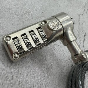 May include: A silver combination lock with a black cable attached. The lock has four dials with numbers 1 through 9. The lock is attached to a black cable.