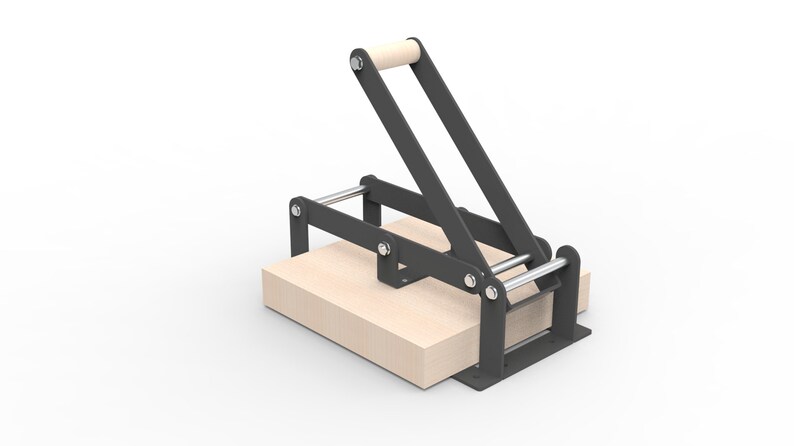 May include: A black metal press with a wooden handle and a light-colored wooden base. The press has a lever-style design and is likely used for pressing materials. The base is rectangular and appears to be made of wood.