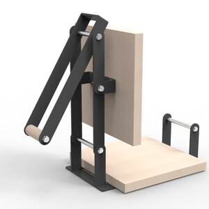 May include: A black and wood press with a light wood base and a vertical wood panel. The press has a lever arm with a wooden handle and is held together with silver bolts.