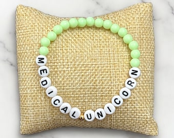 Puede incluir: Un brazalete de cuentas de color verde claro con las palabras "MEDICAL UNICORN" escritas en letras blancas.