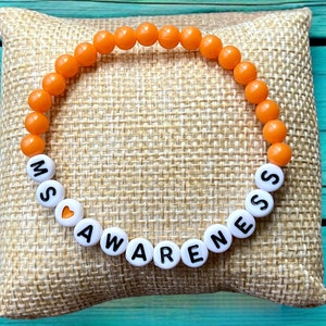 May include: Orange beaded bracelet with white beads spelling "MS AWARENESS" with a small orange heart bead.