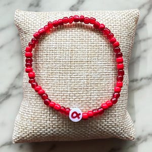 May include: A red beaded bracelet with a white charm featuring the letter "A" in red.