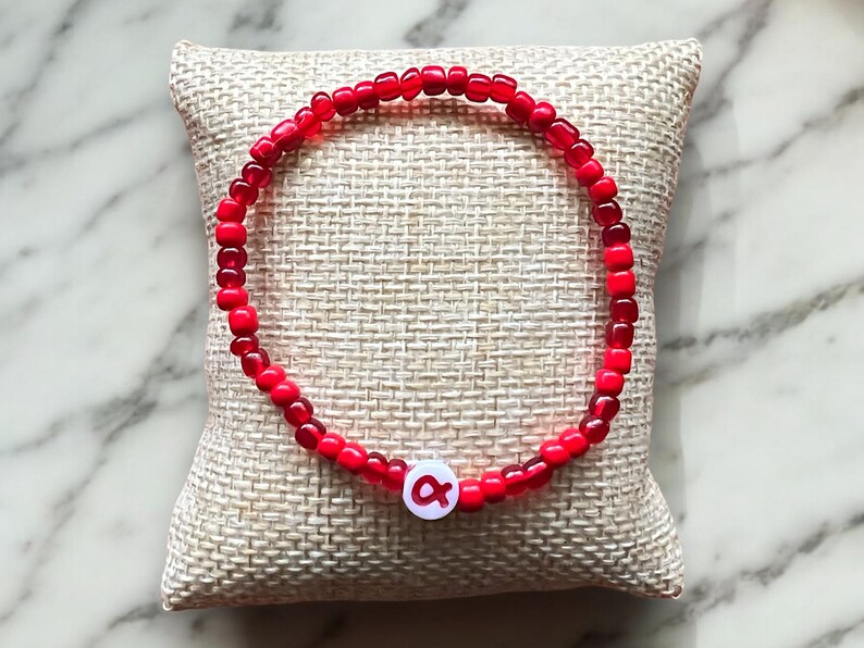 May include: A red beaded bracelet with a white charm featuring the letter "A" in red.