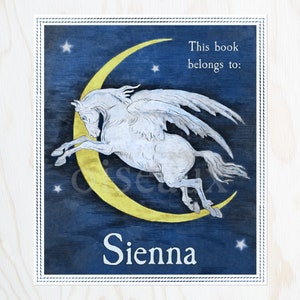 May include: A blue and yellow bookplate with a white winged horse leaping over a crescent moon. The text "This book belongs to:" is above the image and the name "Sienna" is below the image.