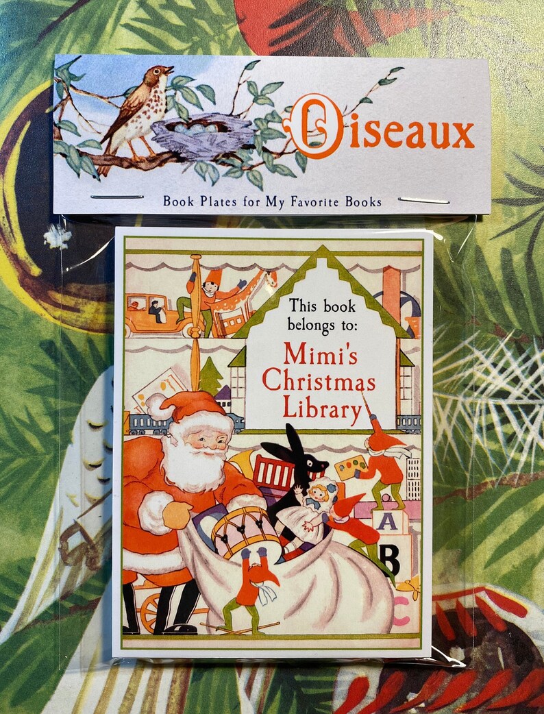 A bookplate featuring a charming vintage illustration of Santa and elves in his workshop. Toys fill the shelves behind them, 2 elves push toys into the sack, 1 stands on blocks and paints the name on a white dollhouse. Name is red, text black