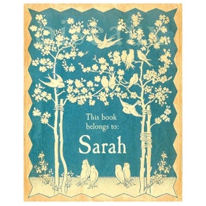 May include: A blue book cover with a white design of two trees with birds and flowers. The text "This book belongs to: Sarah" is printed on the cover.