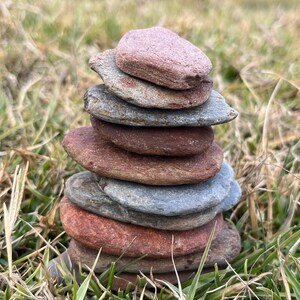 May include: A stack of flat, gray and brown stones balanced on top of each other in a grassy field.