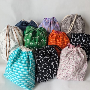 May include: A collection of 10 drawstring bags in various colors and patterns, including floral, geometric, and polka dot designs. The bags are made of fabric and have a white drawstring.