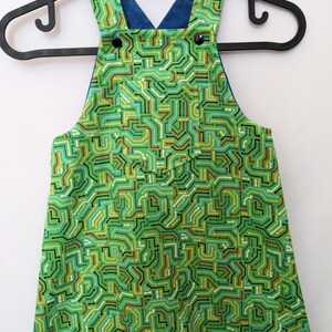 May include: Green overalls with a circuit board pattern. The straps are blue and have black buttons.