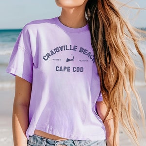 May include: A lavender cropped t-shirt with the text "Craigville Beach Cape Cod 41.6326° N 70.3367° W" printed on the front.