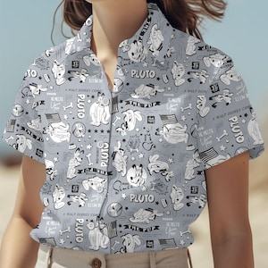 May include: Pale grey button-up shirt with a repeating pattern of Pluto from Disney comics. The design includes Pluto illustrations, stars, bones, and text elements like "PLUTO" and "THE PUP". The shirt has short sleeves.