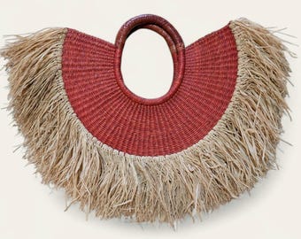 May include: A woven red and tan handbag with a circular handle. The bag features a red centre with a tan fringe around the edges. The handle is a dark brown colour.