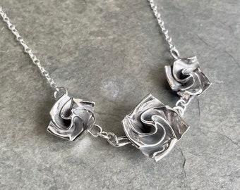 May include: A silver necklace with three silver pendant charms in the shape of a rose. The charms are connected by a silver chain.