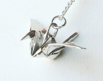 Może przedstawiać: Srebrny naszyjnik z zawieszką w kształcie żurawia origami. Żuraw jest tradycyjnym japońskim symbolem pokoju i szczęścia.