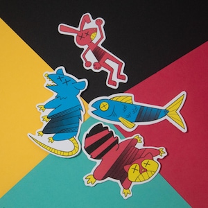 May include: Four colorful stickers featuring cartoon animals with an 'X' over their eyes. The stickers are on a multi-colored background. The animals are a red rabbit, a blue rat, a red and black raccoon, and a blue fish.
