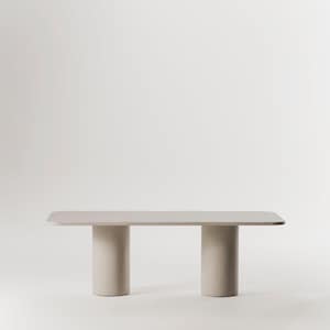 Peut inclure: Une table rectangulaire de salle à manger beige clair avec un plateau lisse et plat et deux pieds cylindriques. La table est sur un fond blanc.