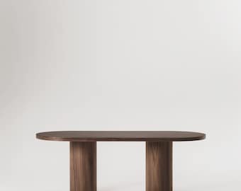 May include: A long, oval-shaped wooden table with two cylindrical legs on each end. The table is made of dark wood with a natural grain pattern.