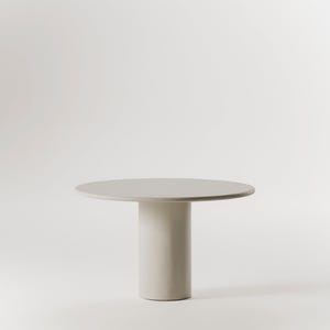 Pode incluir: Uma mesa redonda branca com uma base cilíndrica. A mesa é feita de um material liso e fosco e tem um design simples e moderno.