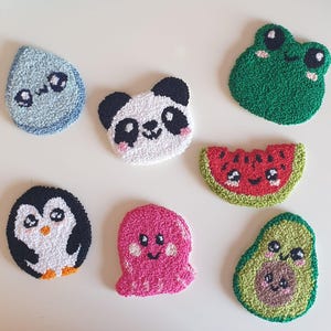 Puede incluir: Una colección de parches bordados a mano y coloridos con varios diseños lindos. Los parches incluyen una gota de lluvia azul, un panda, una rana verde, una rodaja de sandía, un pingüino, un pulpo rosa y un aguacate.