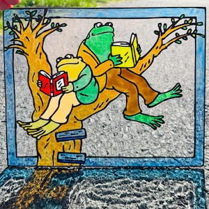 May include: Stained glass art piece featuring two frogs reading books while perched on a tree branch. The frogs are green and yellow, wearing brown pants and jackets. The tree is yellow and brown, set against a textured background.