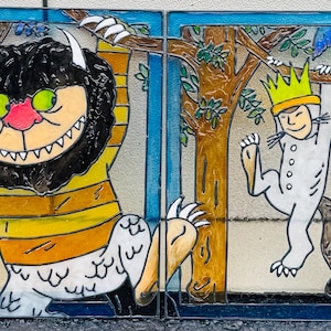 May include: Stained glass panel featuring characters from "Where the Wild Things Are." One panel shows a large, furry creature with a yellow striped shirt. The other panel depicts a child wearing a crown, hanging from a tree.