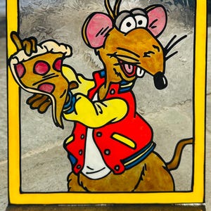 May include: A stained glass panel featuring a cartoon mouse holding a slice of pizza. The mouse wears a red jacket with yellow sleeves and a white shirt. The panel has a yellow border.