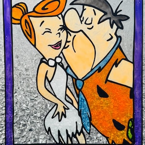 Puede incluir: Panel de vidriera con Fred y Wilma Picapiedra de la caricatura Los Picapiedra. Fred está besando a Wilma, que está sonriendo. El panel tiene un borde púrpura y un fondo de vidrio texturizado. Los personajes están con sus trajes clásicos.