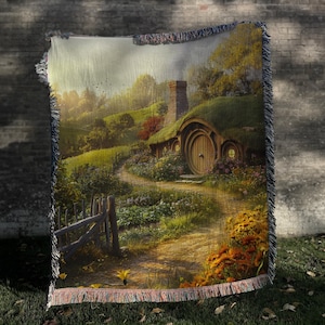 K&ouml;nnte beinhalten: Eine gewebte Wandteppich mit einem fantasievollen Hobbit-Haus mit einer runden T&uuml;r und einem gr&uuml;nen Dach. Das Haus ist umgeben von &uuml;ppigem Gr&uuml;n und einem gewundenen Weg. Der Wandteppich hat ein rustikales, erdiges Gef&uuml;hl.