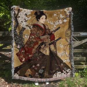 Könnte beinhalten: Eine gewebte Wanddecke aus Tapisserie mit einer japanischen Frau in einem traditionellen Kimono, die zwei Schwerter hält. Der Hintergrund ist gold- und braunfarben mit weißen Kirschblüten.