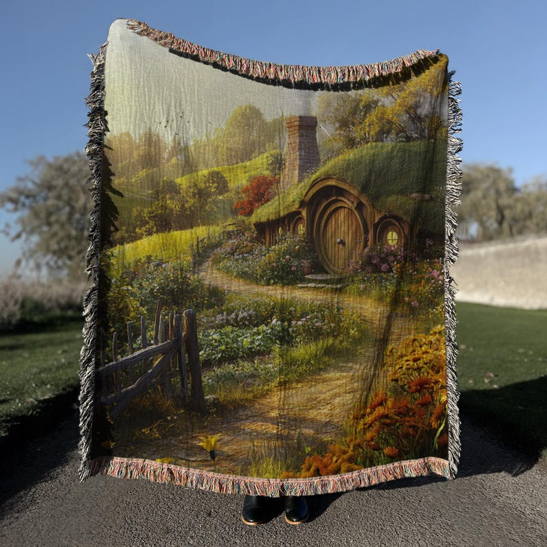 K&ouml;nnte beinhalten: Eine gewebte Wanddecke aus Tapisserie mit einer fantasievollen Illustration eines Hobbit-Hauses mit einer runden T&uuml;r und einem &uuml;ppigen gr&uuml;nen Garten. Das Haus ist von Blumen und einem gewundenen Weg umgeben.