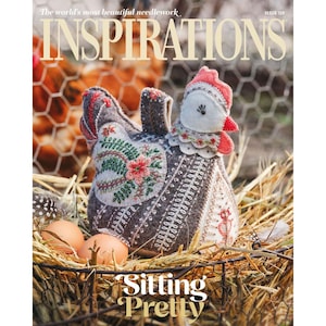 Pode incluir: A capa da revista Inspirations, edição 129, apresenta uma galinha artesanal com detalhes bordados. A galinha é cinza e marrom com crista e barbela vermelhas, em uma cesta com ovos e feno. O texto "Sitting Pretty" está na parte inferior.