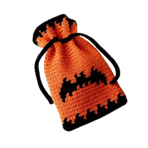 May include: An orange crocheted drawstring bag with black accents, resembling a jack-o'-lantern. The bag features a black rim and a jagged black pattern along the bottom, with black drawstrings. This handmade bag is perfect for Halloween.