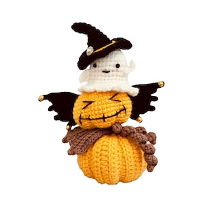 May include: A handmade crochet Halloween decoration featuring a smiling jack-o'-lantern with a ghost wearing a witch hat. The pumpkin is orange, the ghost is white, and the hat is black. The decoration has black wings and a brown scarf.