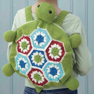 May include: A green crochet turtle backpack with a colorful geometric design on the shell. The backpack features a turtle head, four flipper-like appendages, and adjustable straps. The shell design includes red, white, blue, and green hexagonal patterns.