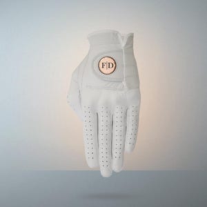 以下が含まれることがあります： 白のゴルフグローブ。手のひらと指には穴が開いています。グローブには、銅色のフレームに「F D」のイニシャルが入った円形のエンブレムが付いています。右利きゴルファー向けに設計されています。