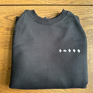 May include: Black sweatshirt with a white arrow design on the front. The arrows point up, right, down, and down.